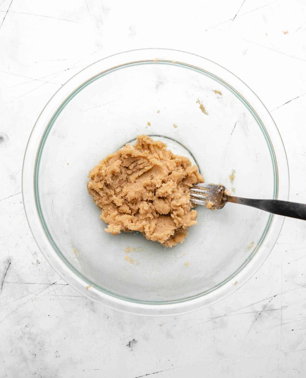 A fork mixing butter and brown sugar in a glass mixing bowl.