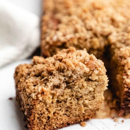 A slice of banana crumb cake at an angle next to the cake.