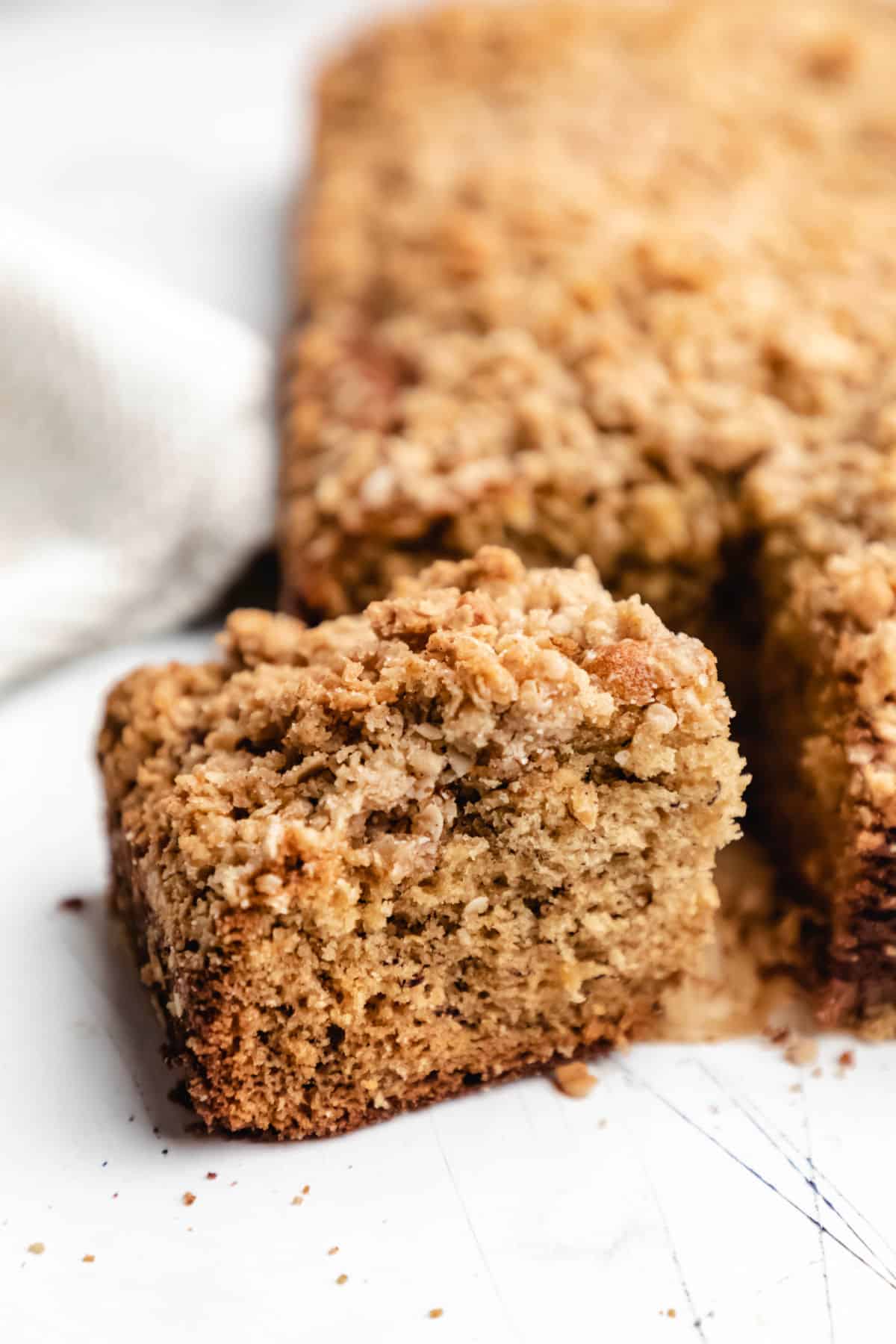 A slice of banana crumb cake at an angle next to the cake.