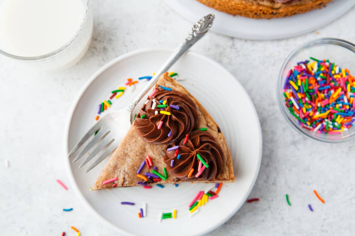 A slice of chocolate chip cookie cake on a white plate with a silver fork. 