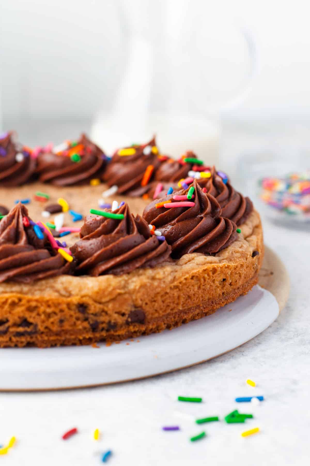 Close up view of chocolate chip cookie cake topped with swirls of chocolate buttercream and sprinkles.