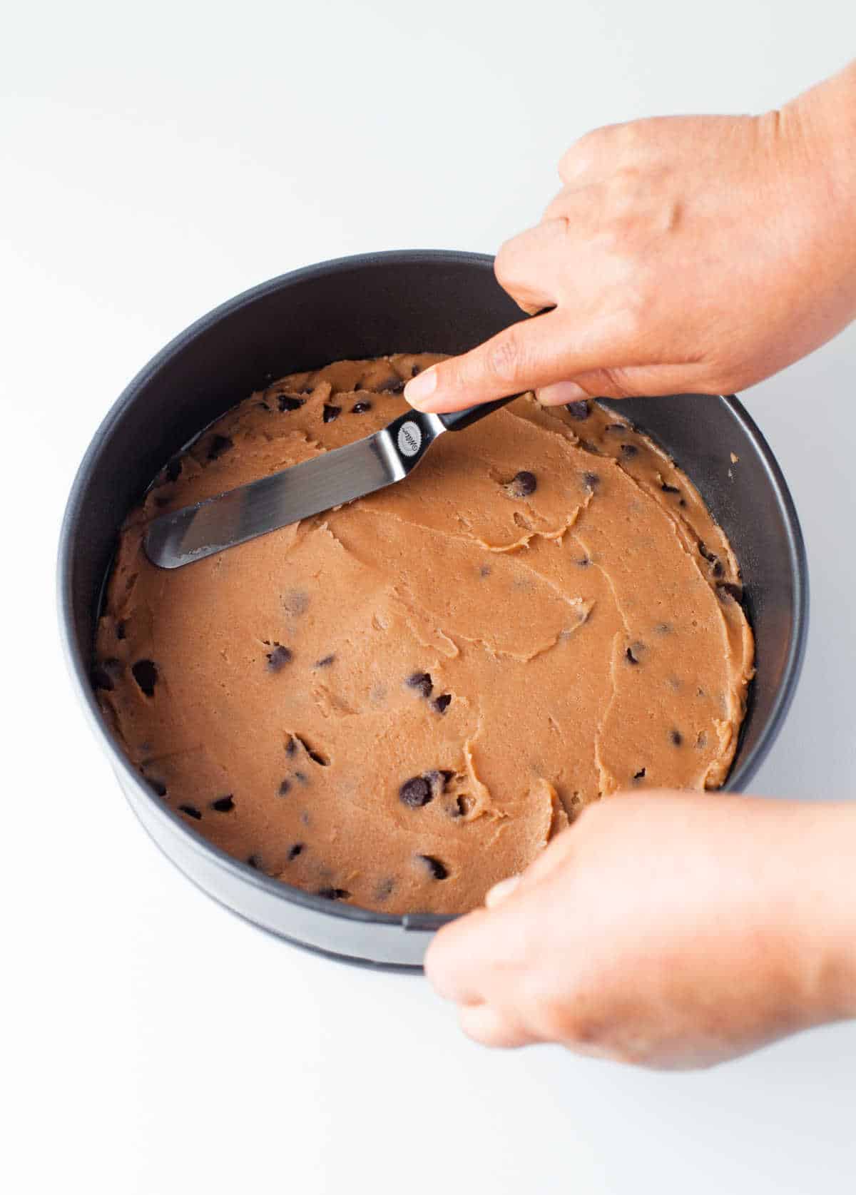An offset spatula spreading cookie dough into a springform pan.
