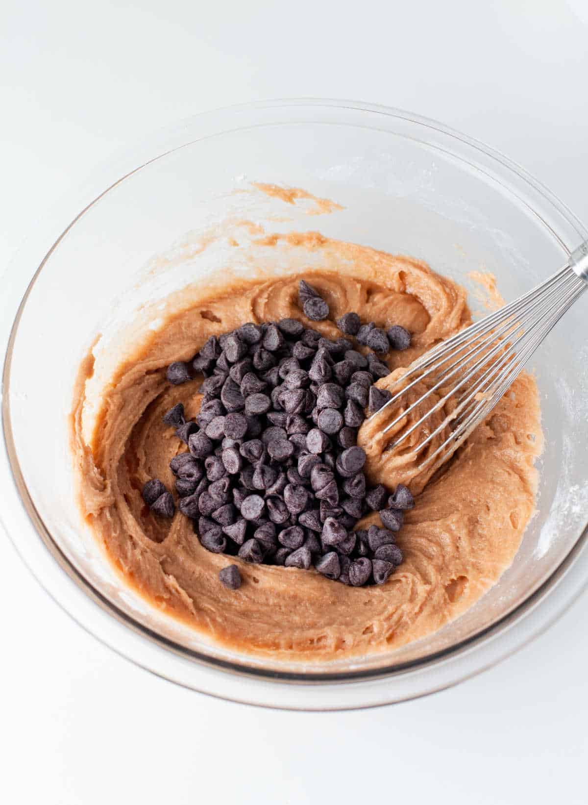 A whisk stirring chocolate chips into cookie dough. 