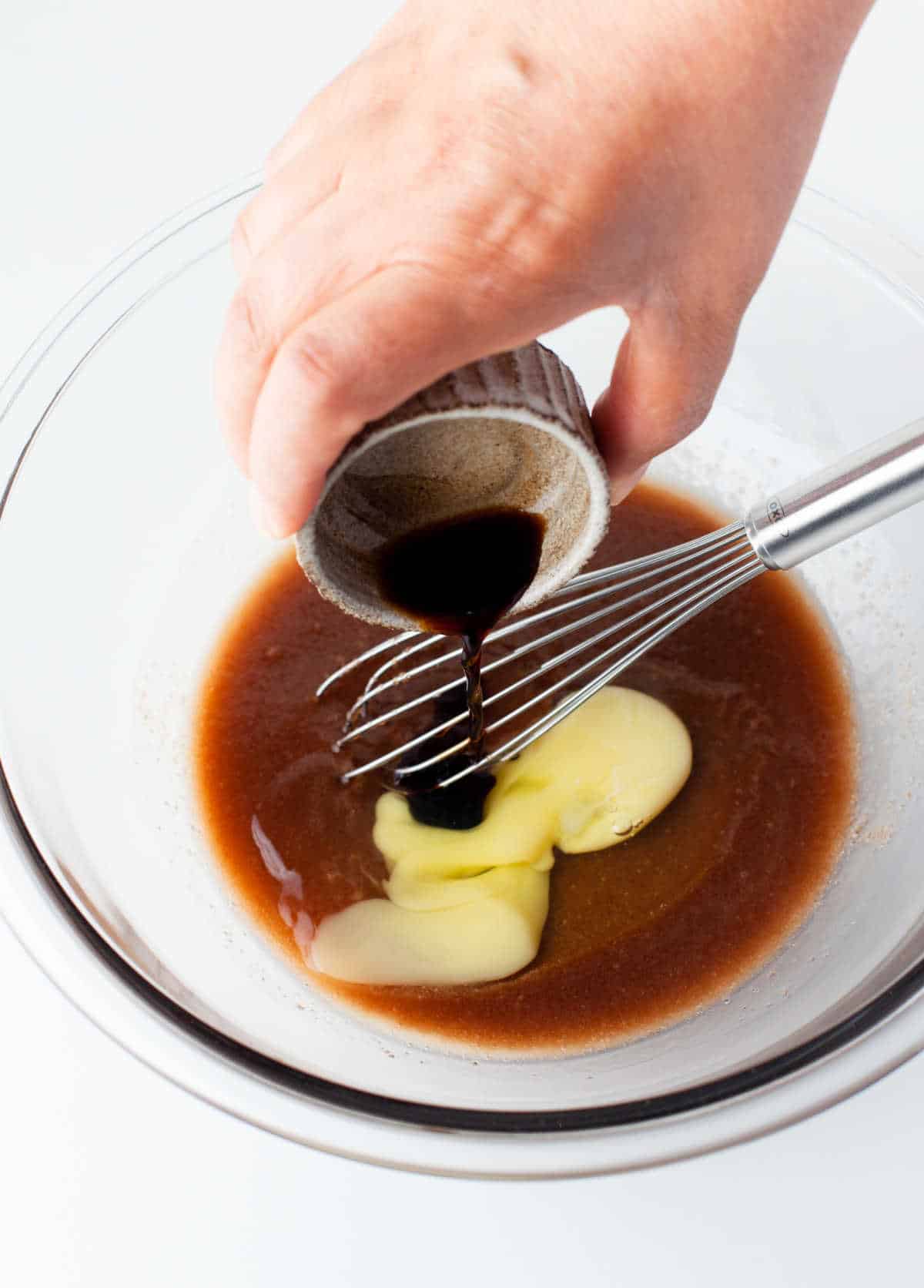 A dish pouring vanilla into a bowl of egg an sugar mixture. 