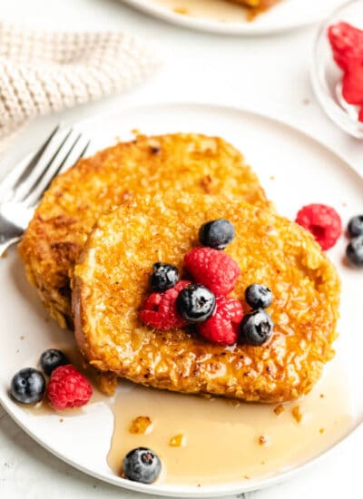 A plate of cornflake French toast with blueberries and raspberries on it.