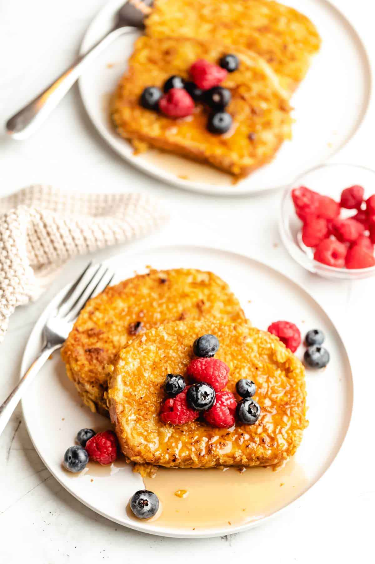 Two plates of cornflake French toast with berries. 