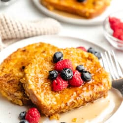 Two pieces of cornflake French toast on a plate in front of another plate of French toast.