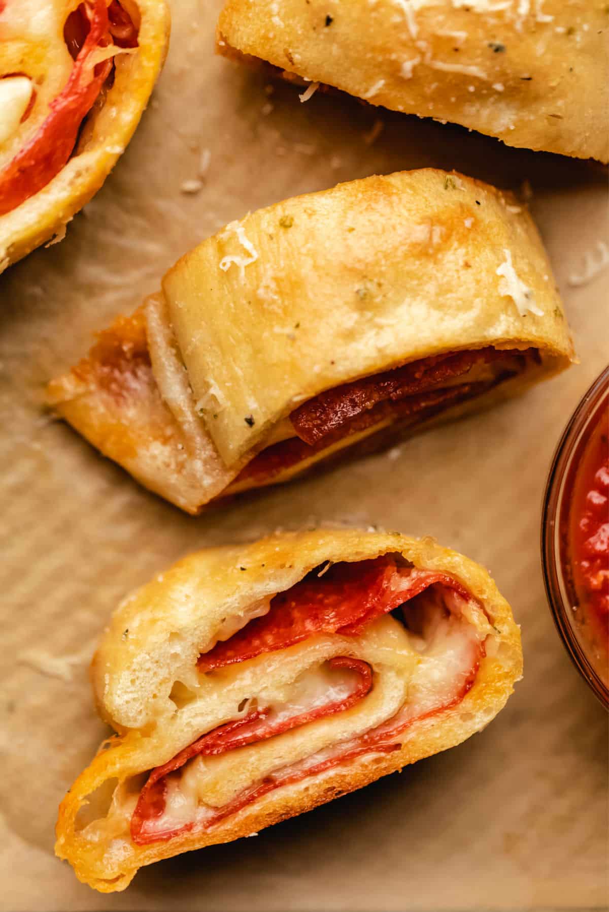 Slices of pepperoni bread on brown parchment paper next to pizza sauce. 