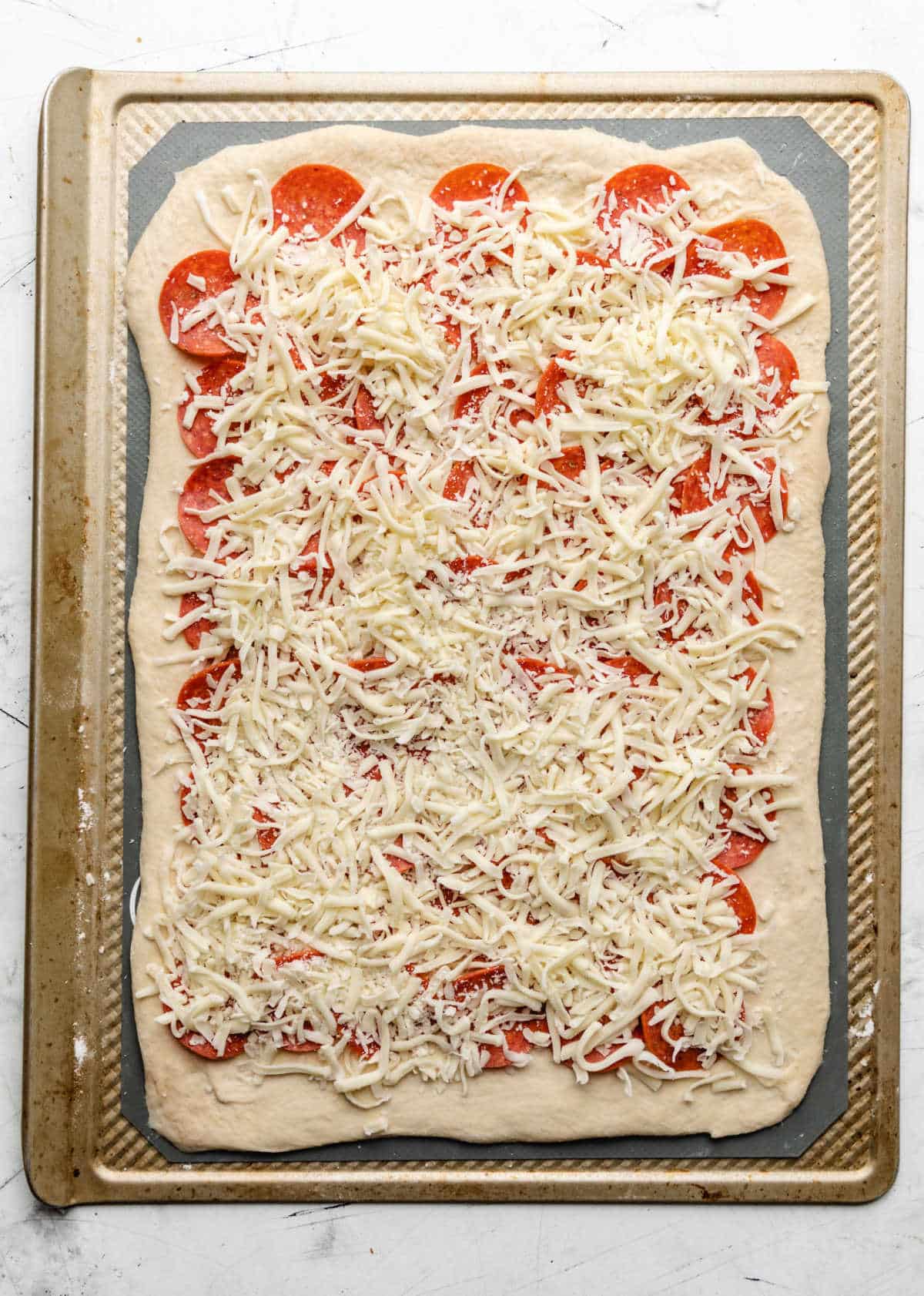 A layer of shredded mozzarella over pepperonis on pizza dough.