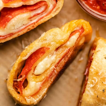 Three pieces of pepperoni bread next to a dish of pizza sauce.