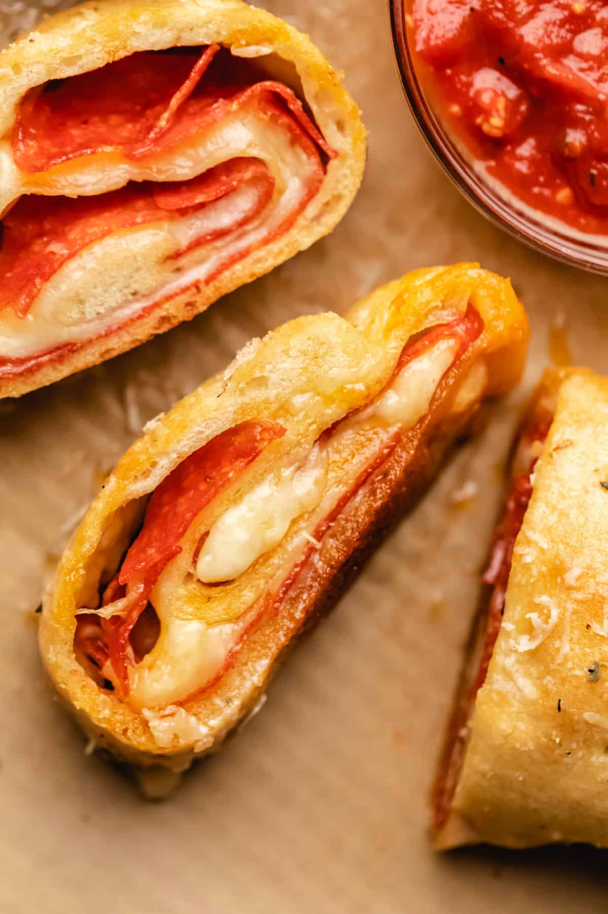 Three pieces of pepperoni bread next to a dish of pizza sauce.