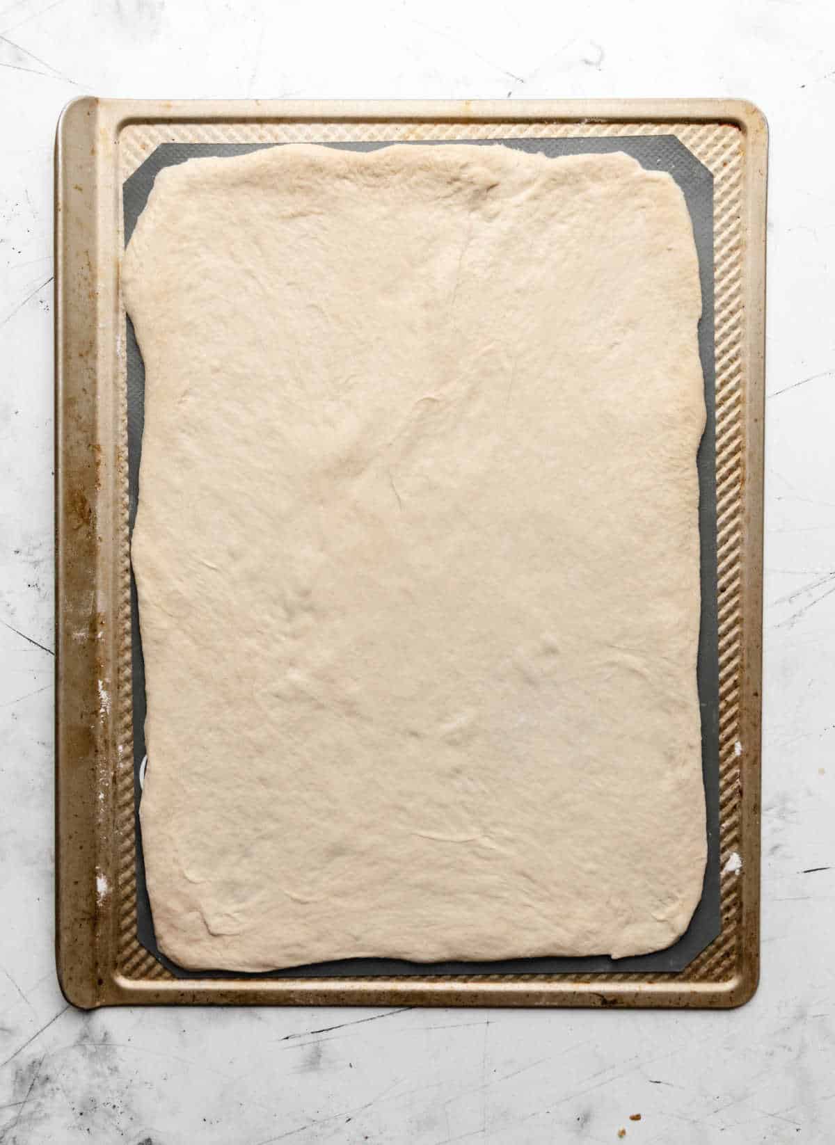 Pizza dough stretched out on a silicone baking liner. 