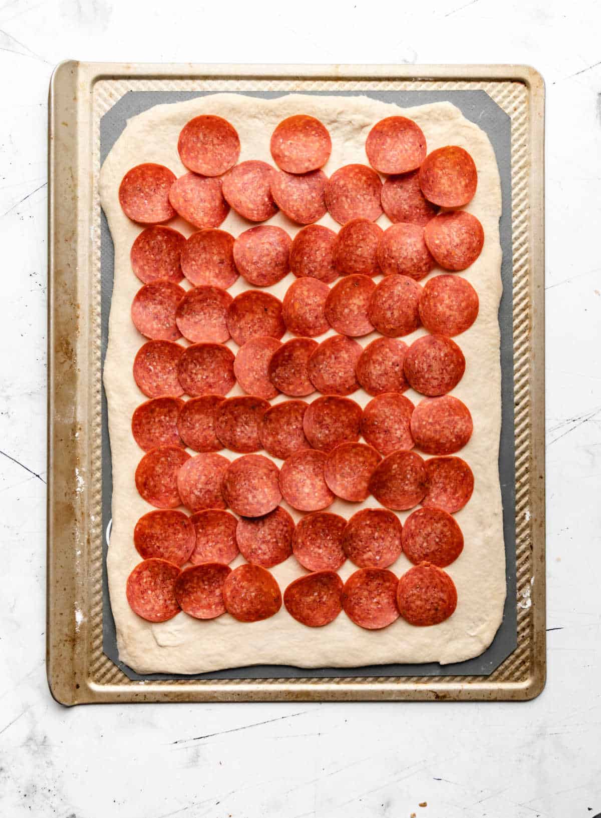 A layer of sliced pepperonis on pizza dough.