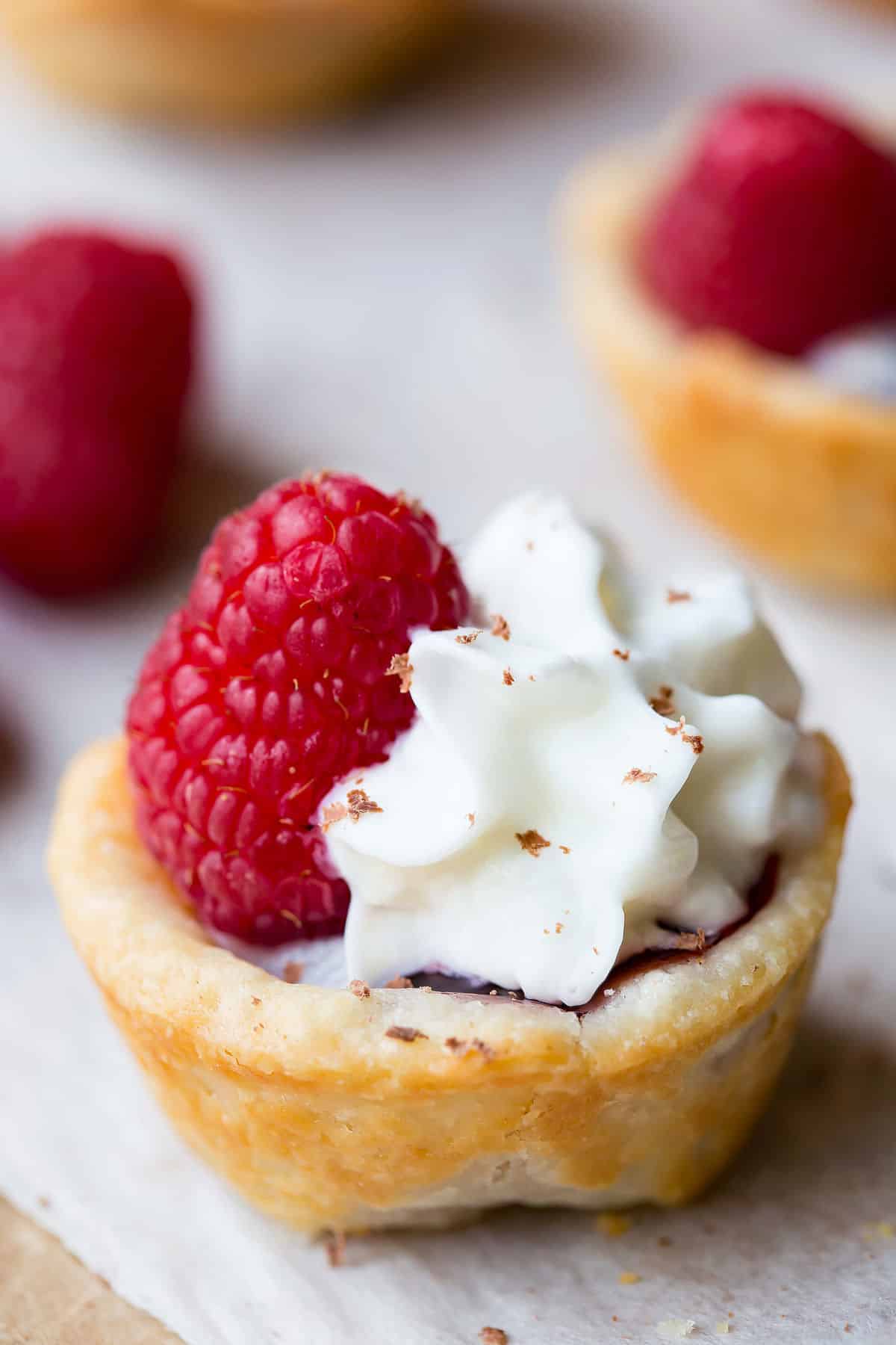 A raspberry tassie topped with whipped cream and a raspberry.