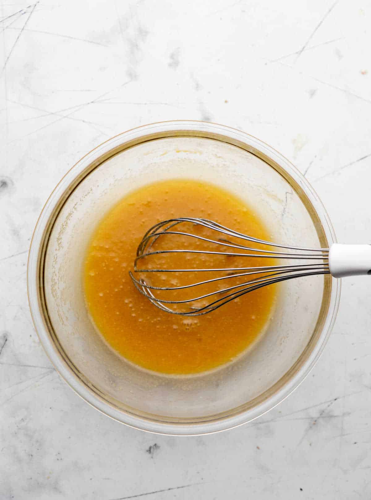 Melted butter and sugars whisked together in a glass mixing bowl. 