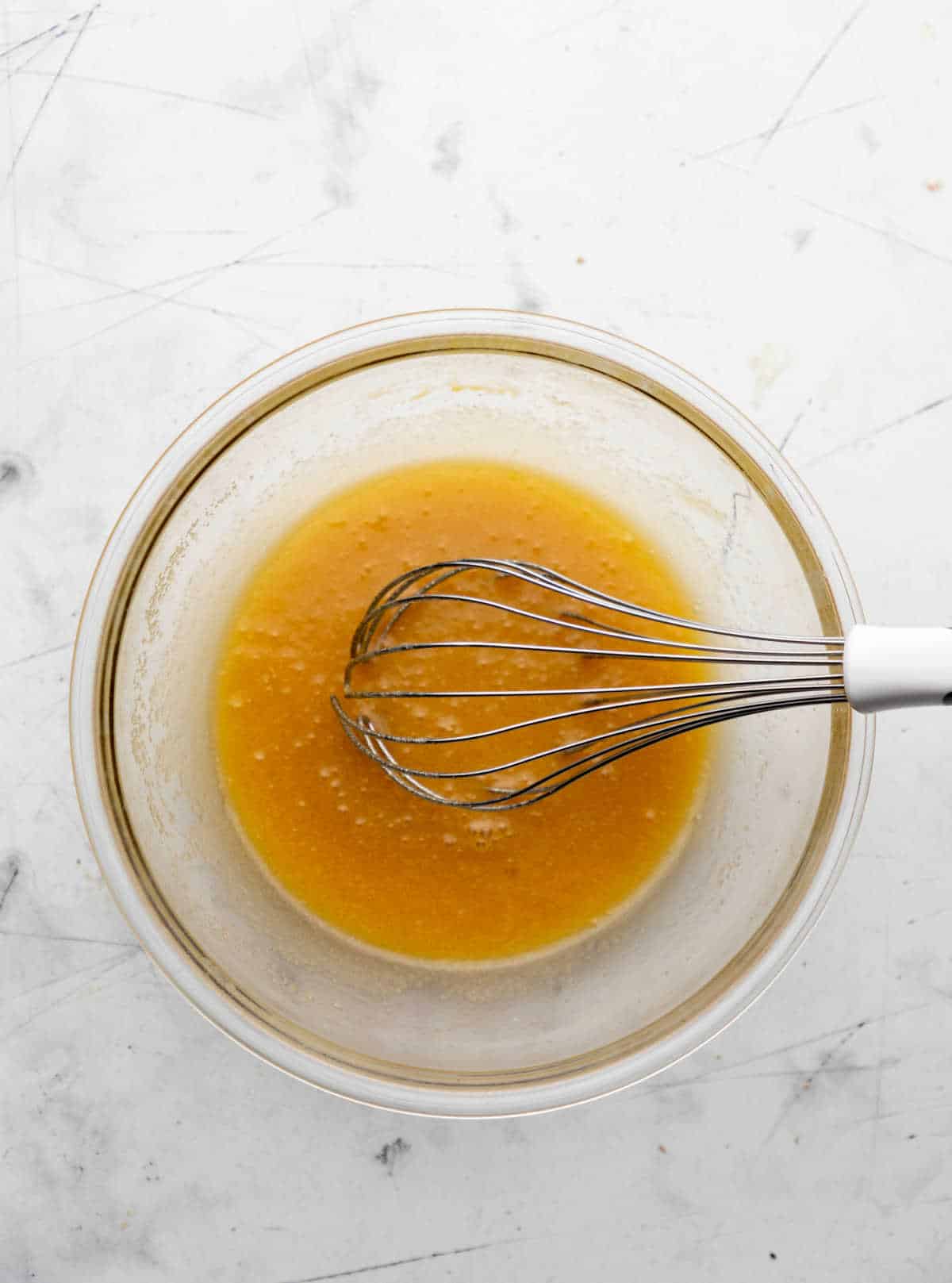 Melted butter and sugars whisked together in a glass mixing bowl.