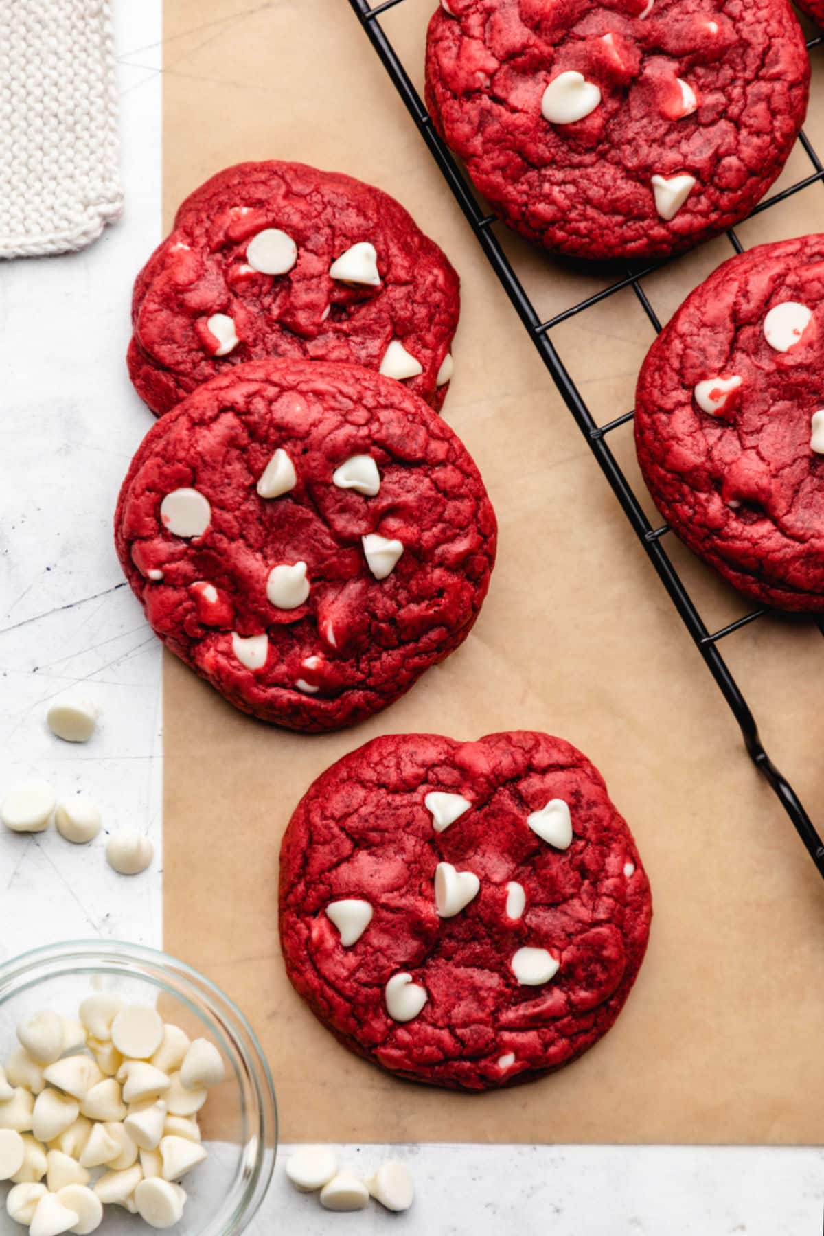 Three red velvet cookies overlapping on a piece of brown parchment paper.