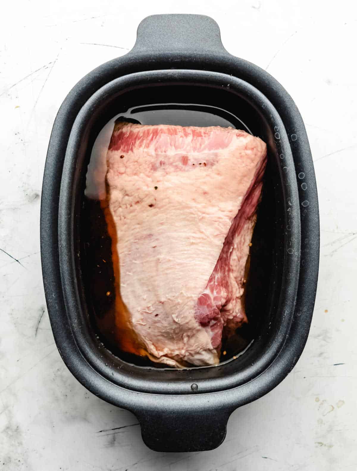 A corned beef brisket in beer and beef broth in a slow cooker. 