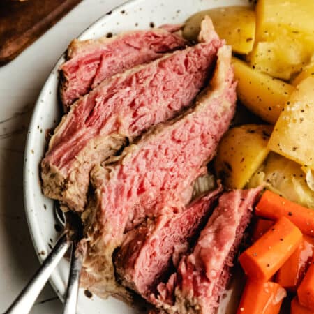 Slices of slow cooker corned beef next to carrots and potatoes.