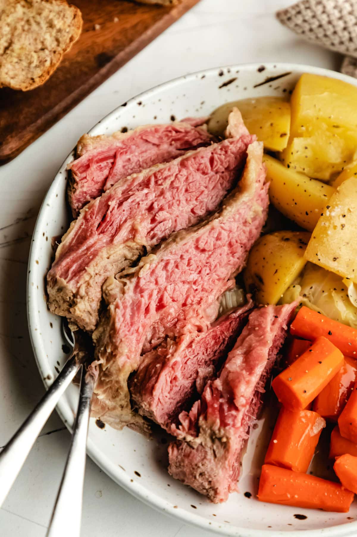 Slices of slow cooker corned beef next to carrots and potatoes. 