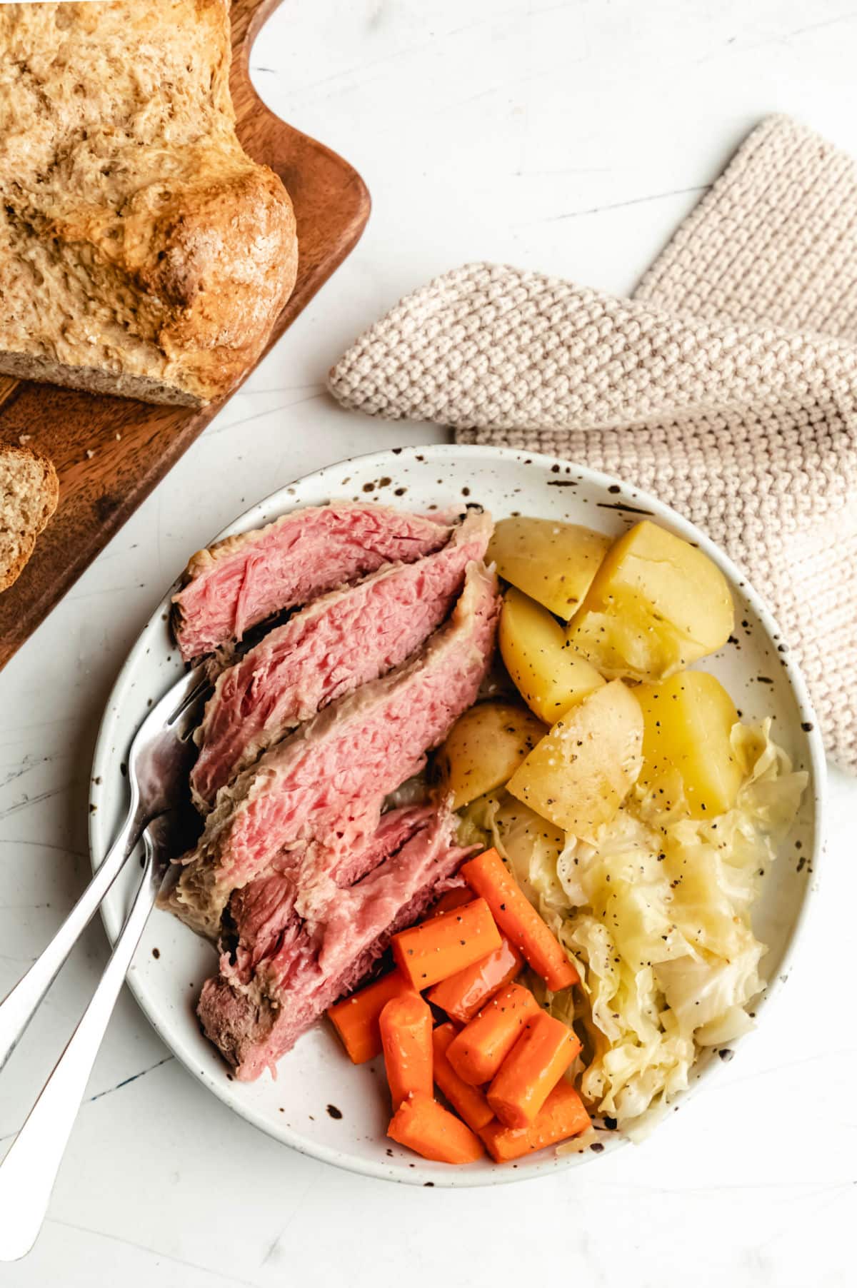 A plate of sliced corned beef, cabbage, potatoes, and carrots next to a knit napkin. 