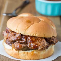 Slow cooker Texas brisket on a bun next to a dish of barbecue sauce.