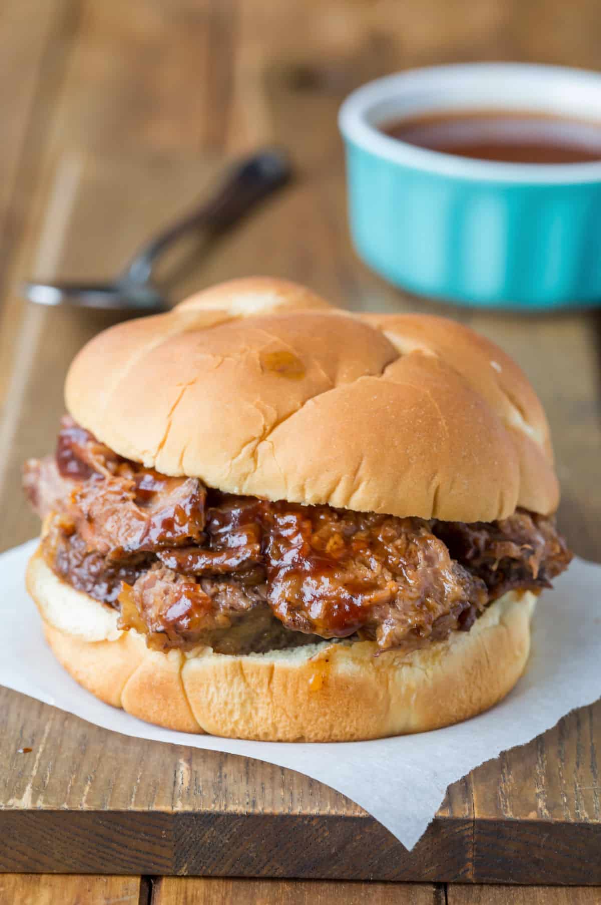 Slow cooker Texas brisket on a bun next to a dish of barbecue sauce.