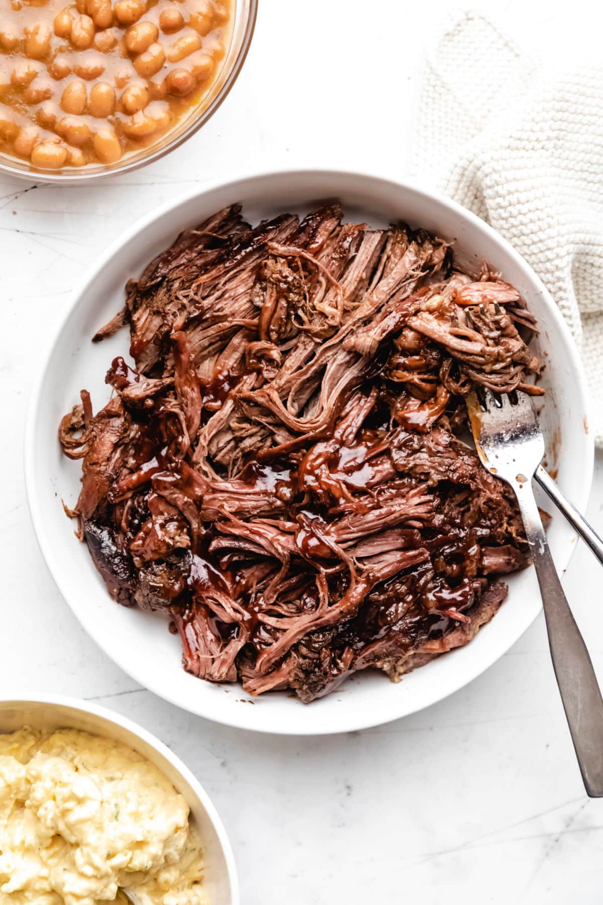 A white dish with two forks in shredded beef brisket.