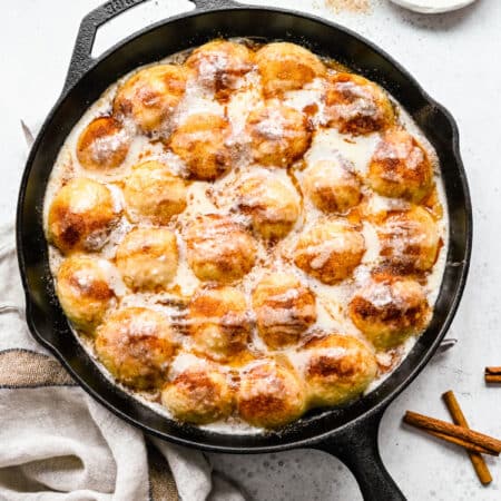 Cinnamon roll bites in a cast iron skillet next to a dish of cinnamon sugar.