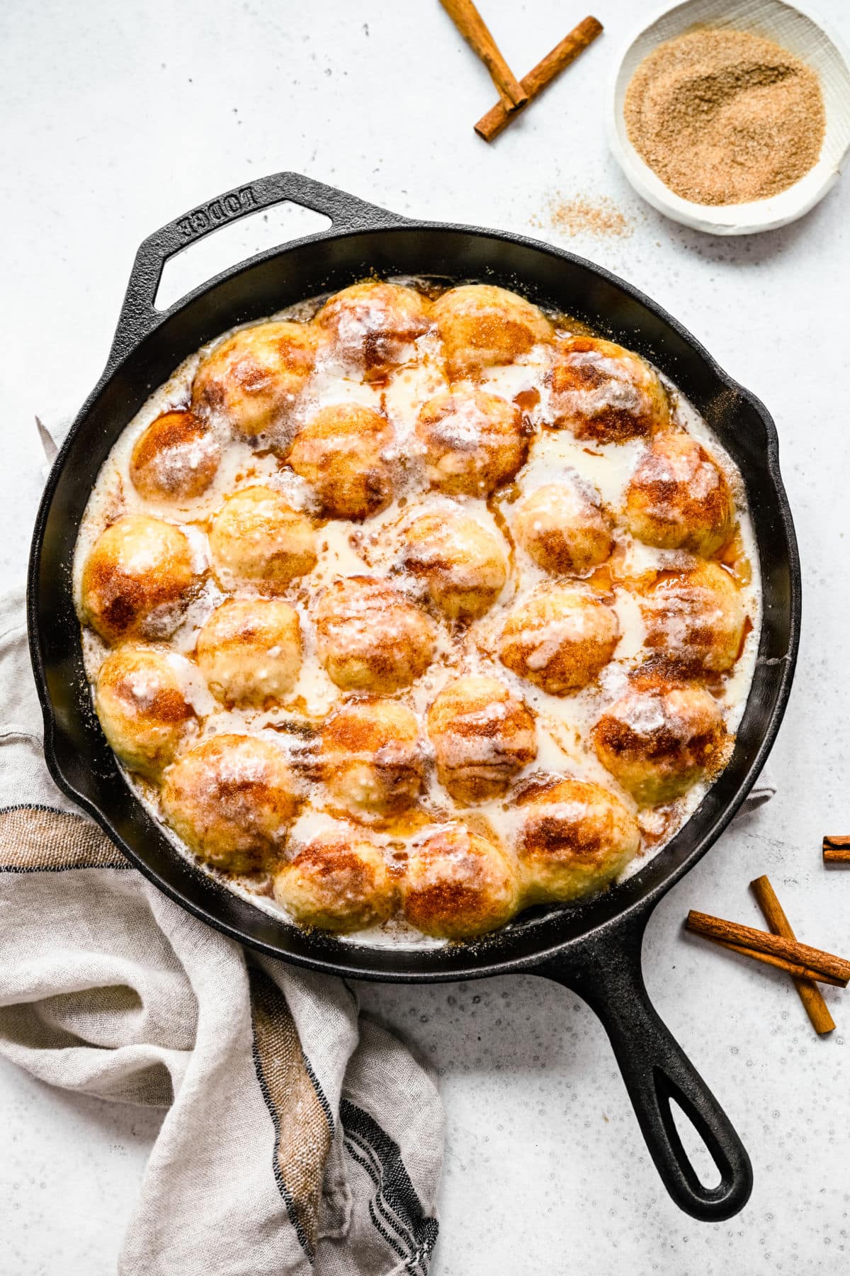 Cinnamon roll bites in a cast iron skillet next to a dish of cinnamon and sugar. 