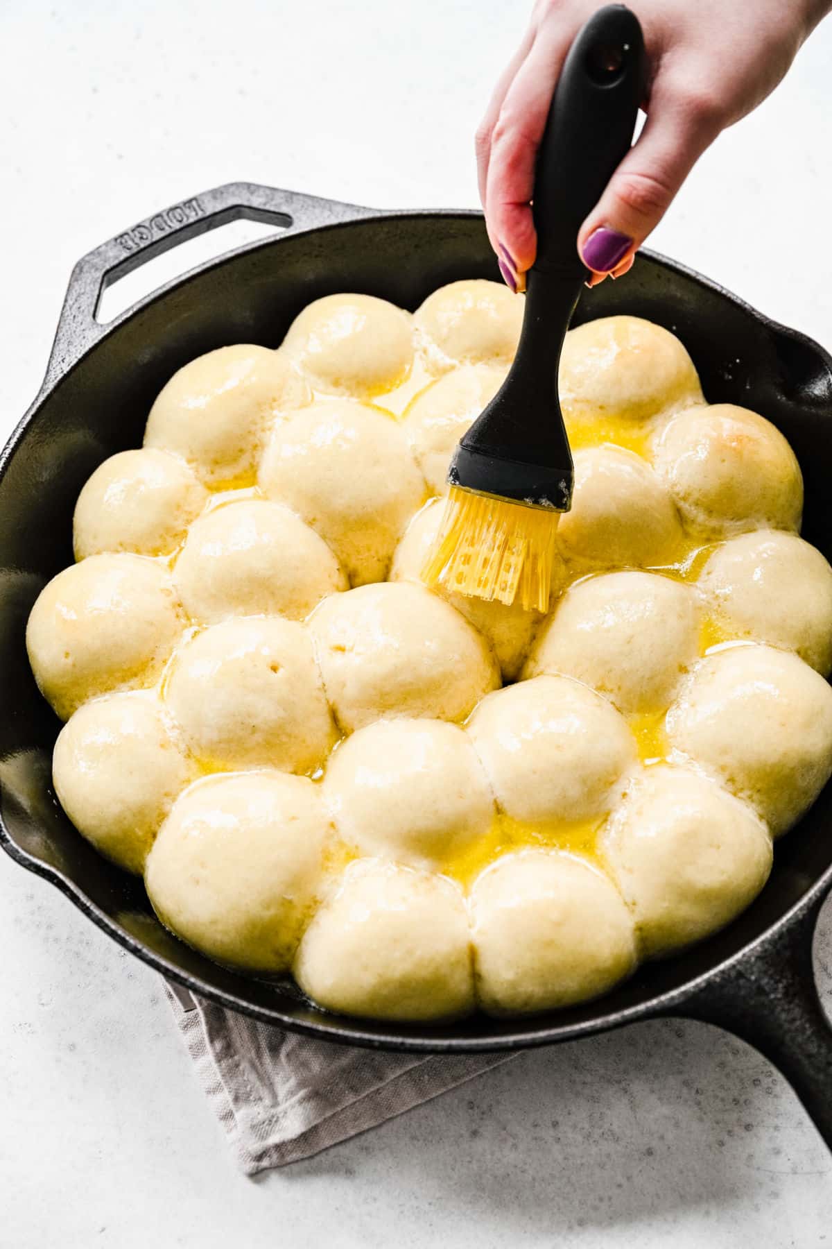 A basting brush brushing butter onto cinnamon roll bites. 