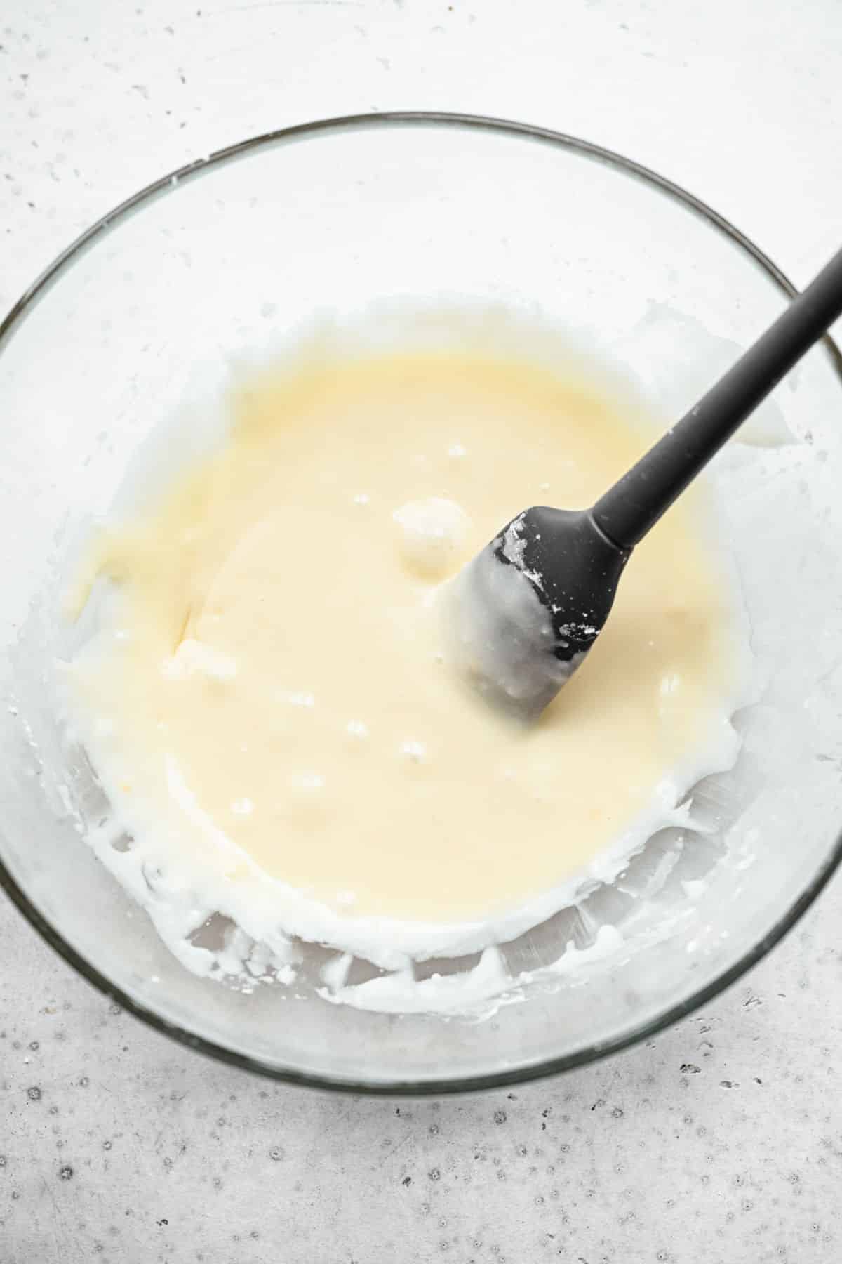 Cinnamon roll bites icing in a glass mixing bowl. 