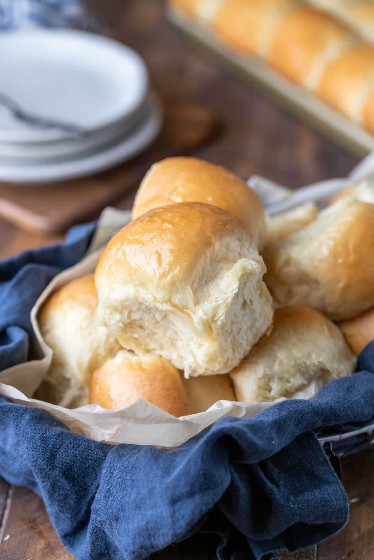 A basket of dinner rolls next to a stack of plates. 