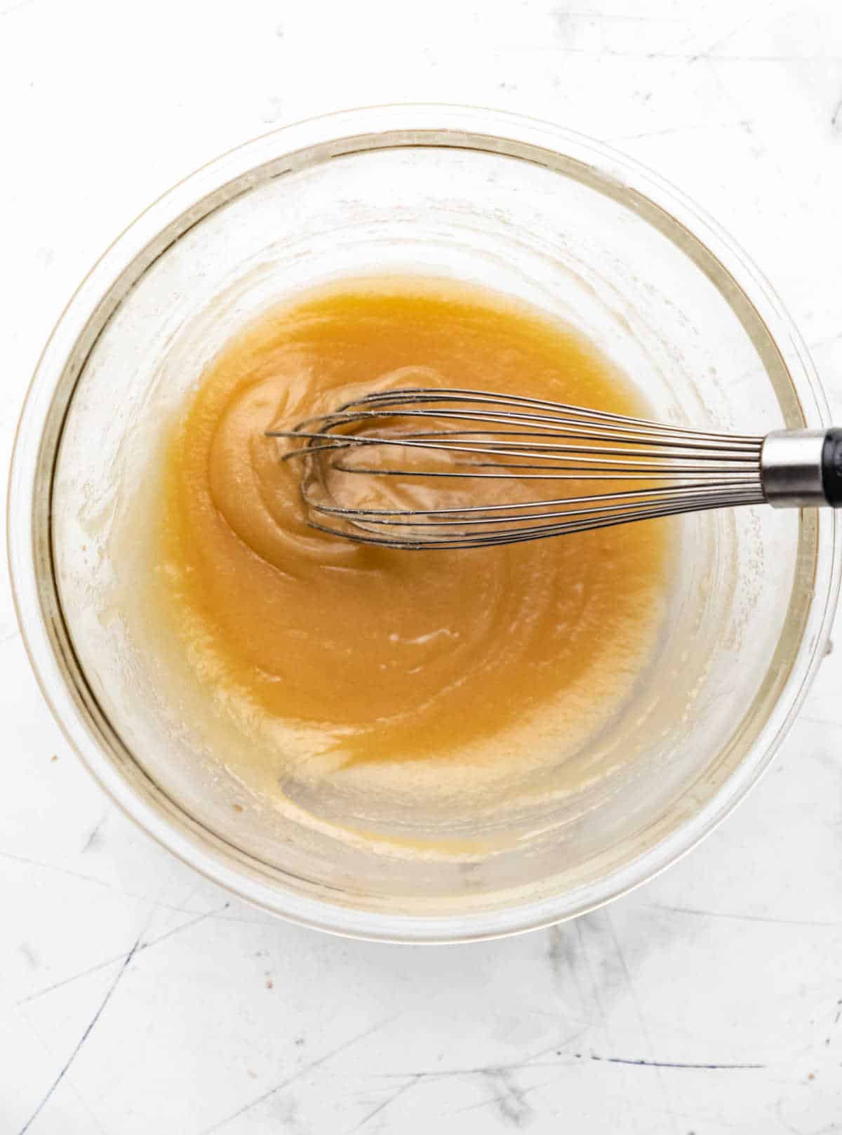 Egg and vanilla whisked into butter sugar mixture in a glass mixing bowl. 