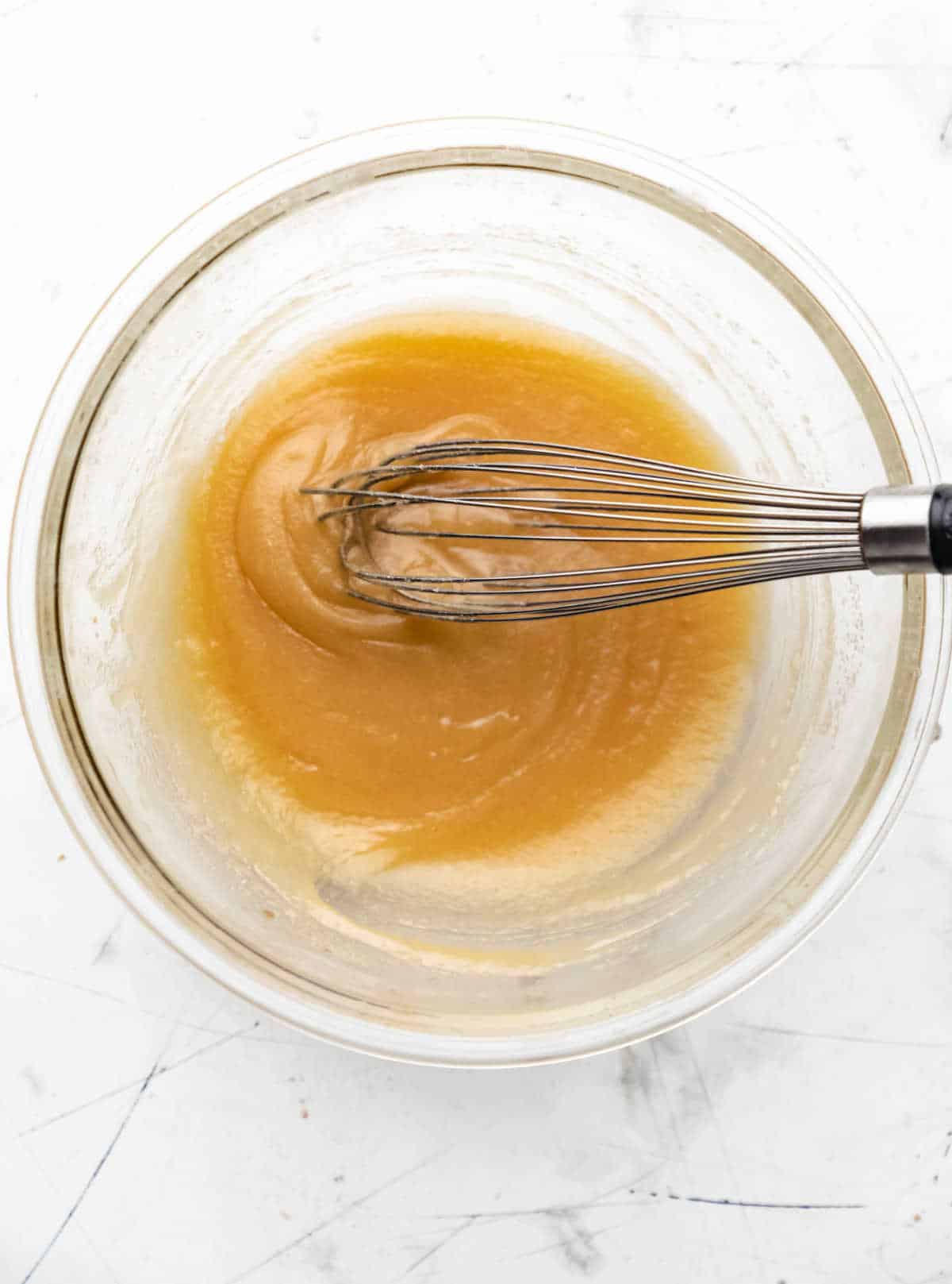 Egg and vanilla whisked into butter sugar mixture in a glass mixing bowl.