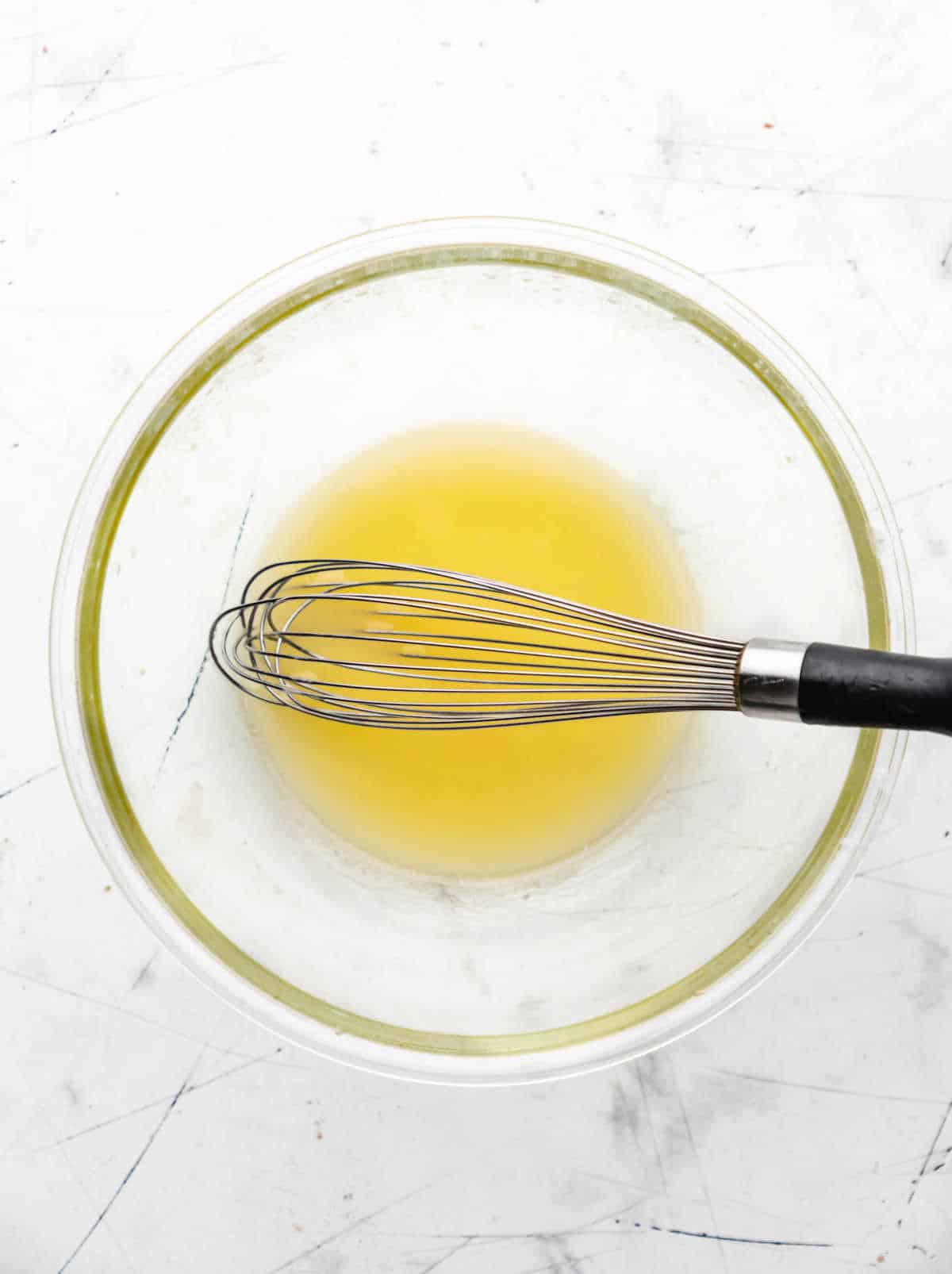 A whisk in a mixing bowl filled with melted butter. 