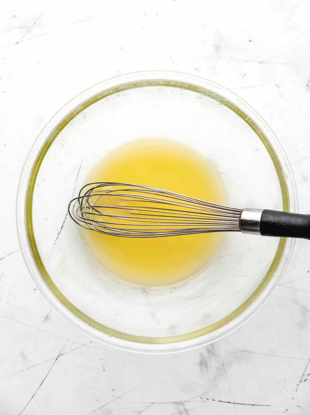 A whisk in a mixing bowl filled with melted butter.