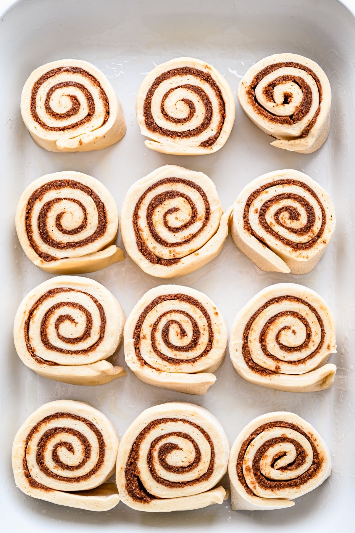Unbaked cinnamon rolls in a white baking pan. 