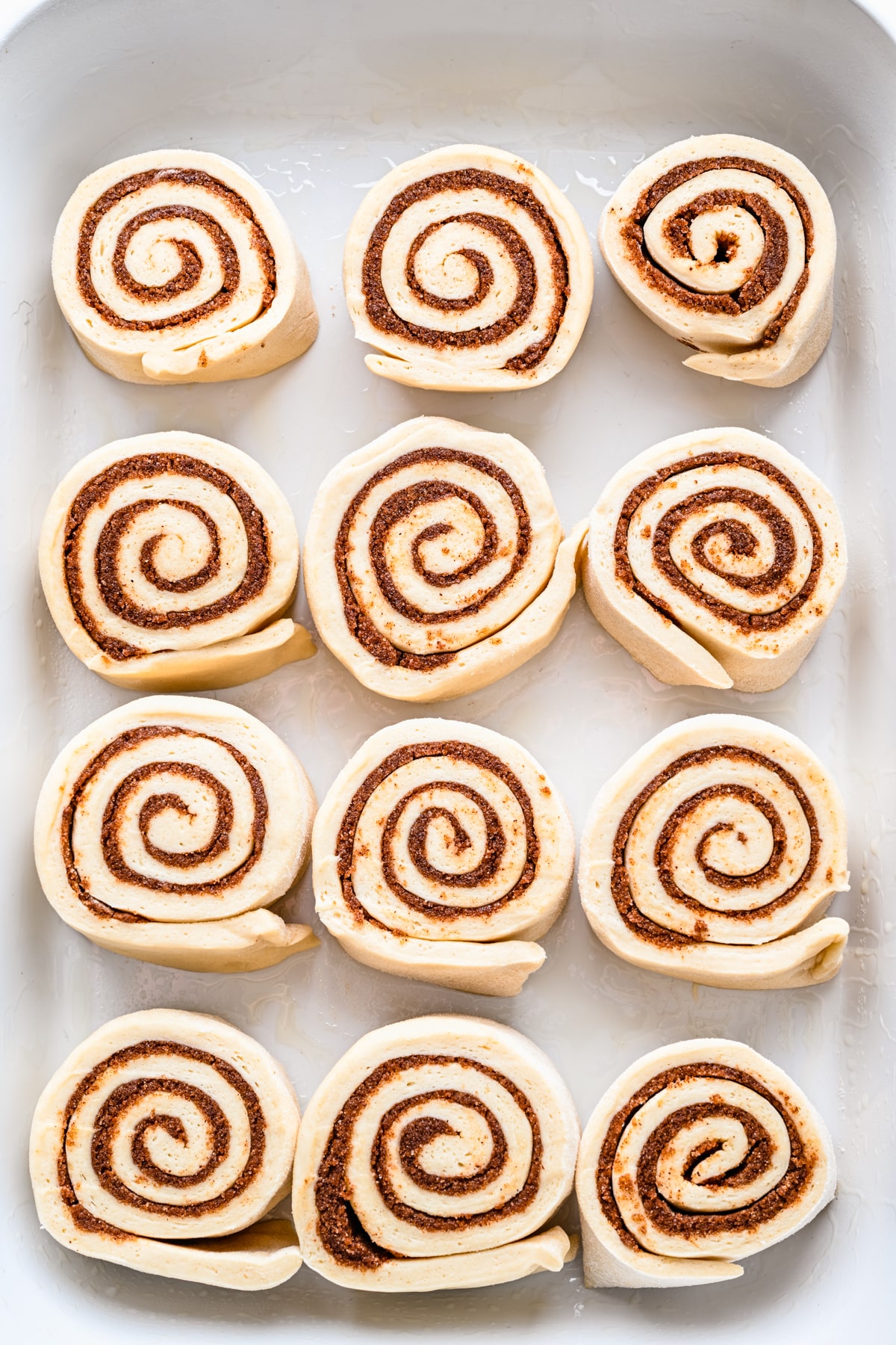 Unbaked cinnamon rolls in a white baking pan.