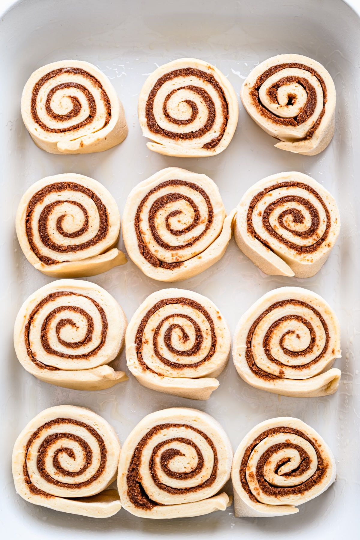 Unbaked cinnamon rolls in a white baking pan. 