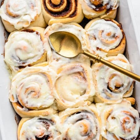 A pan of frosted cinnamon rolls with one cinnamon roll unfrosted.