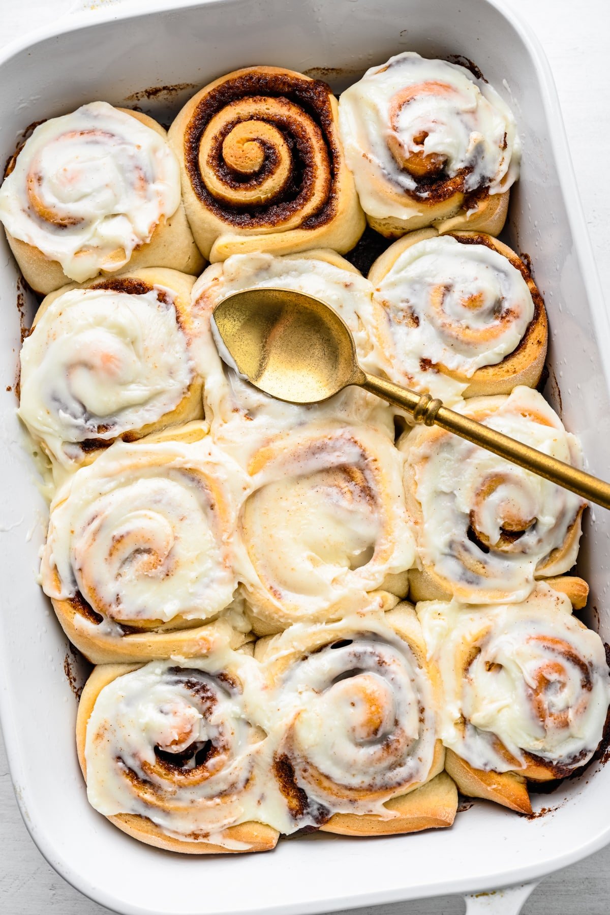 A pan of frosted cinnamon rolls with one unfrosted cinnamon roll. 