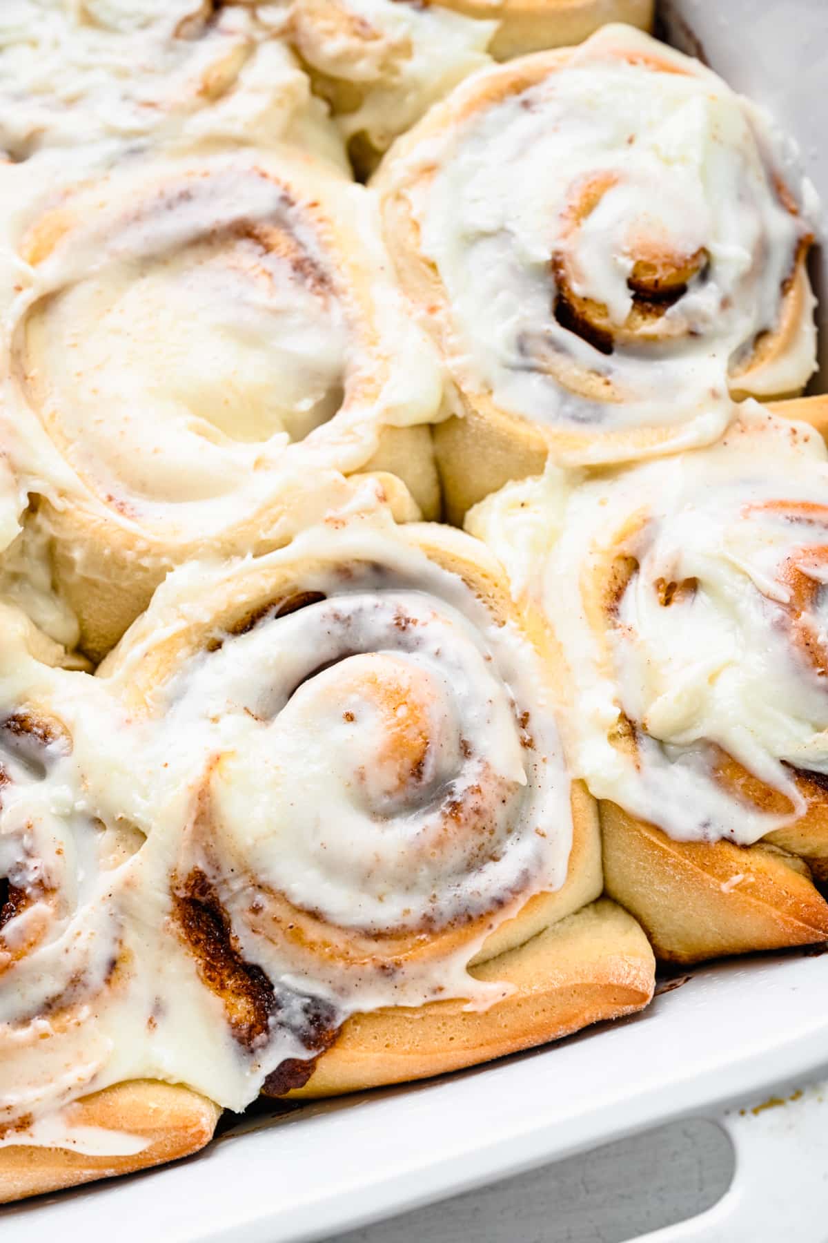 Close up photo of frosted cinnamon rolls in a white pan.