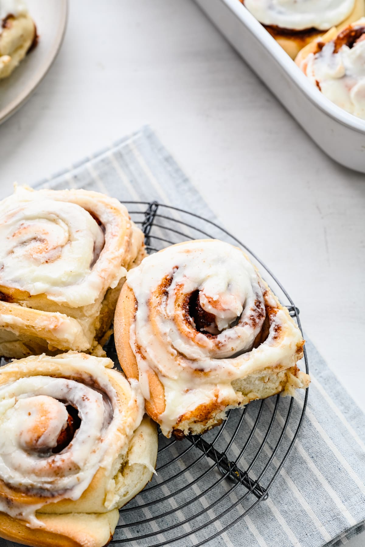 One Hour Cinnamon Rolls Three cinnamon rolls on a wire cooling rack over a striped linen.