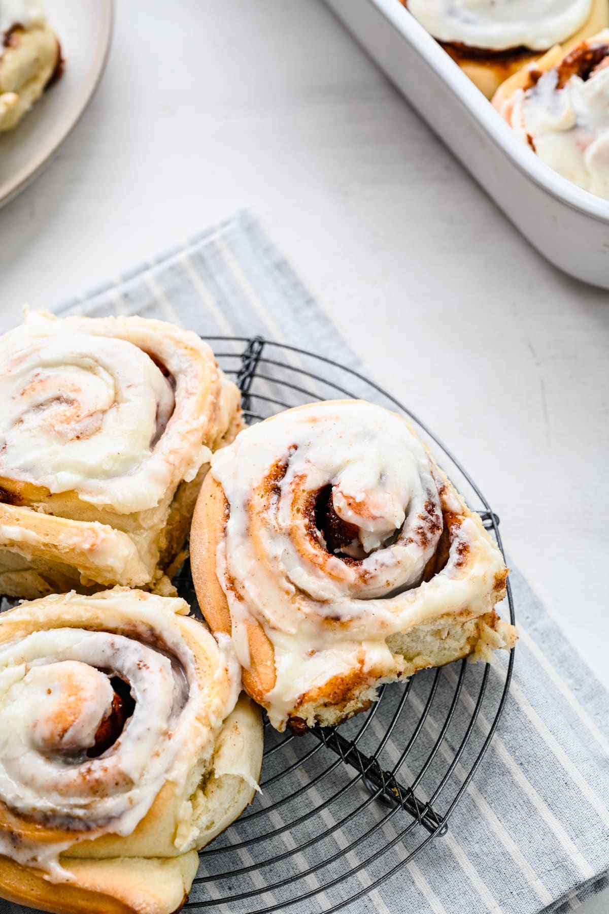 Three cinnamon rolls on a wire cooling rack over a striped linen.