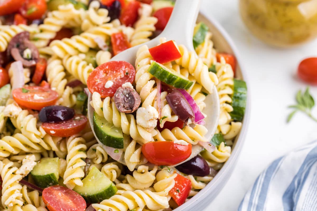 Close up photo of a white spoon holding a scoop of Greek pasta salad.