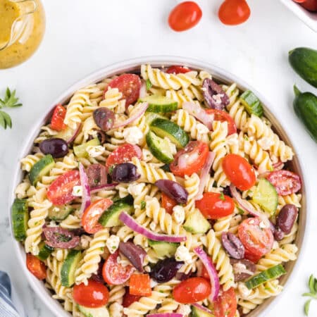 Greek pasta salad surrounded by grape tomatoes and cucumber.