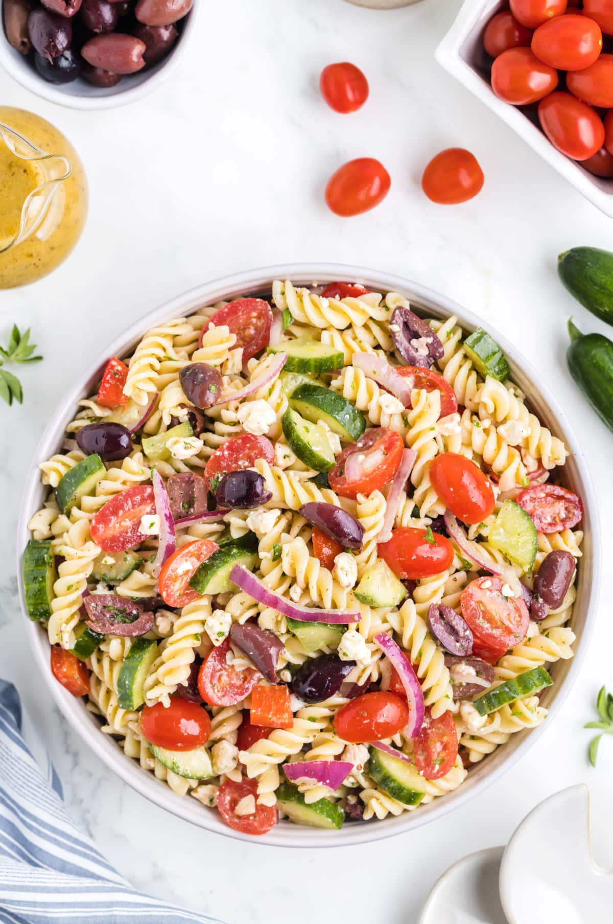 Greek pasta salad surrounded by grape tomatoes and cucumber. 