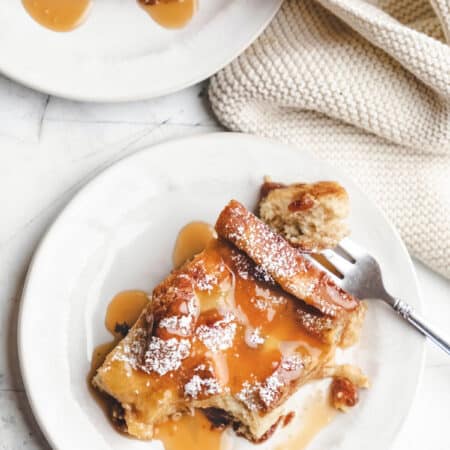 Two plates of Irish bread pudding topped with caramel on two white plates.
