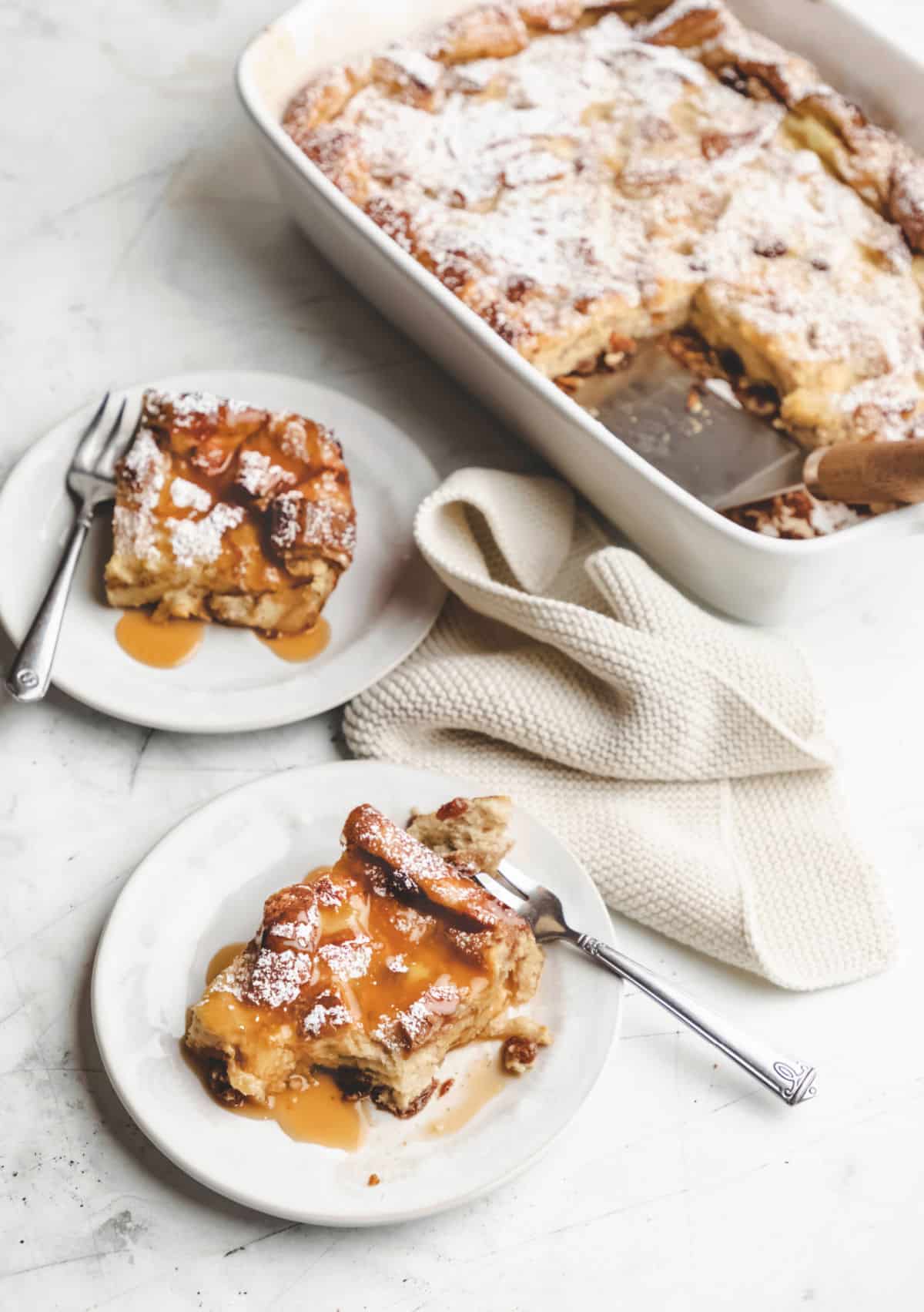 Two plates of Irish bread pudding topped with caramel sauce on white plates.